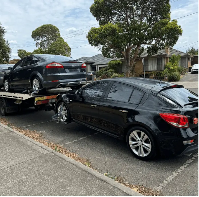 Free car removal in Melbourne service towing a black damaged sedan while another vehicle is loaded on a flatbed truck